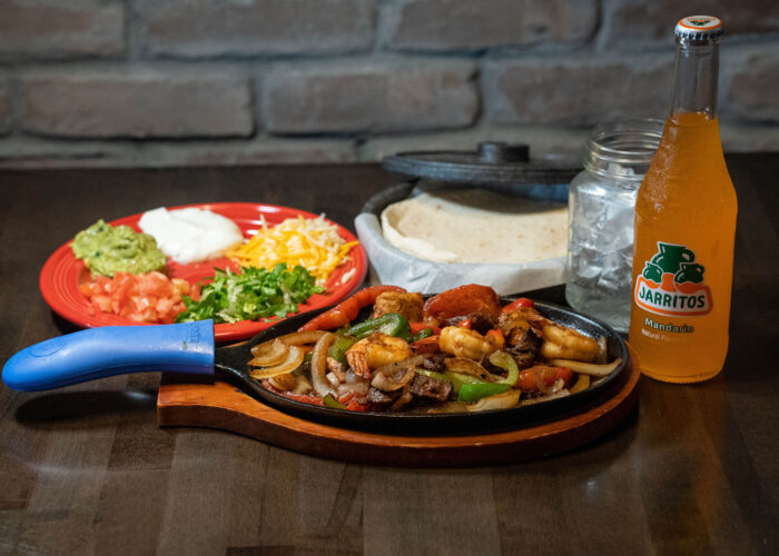 Shrimp And Beef Fajitas On A Table With Fixings And Cold Beverage